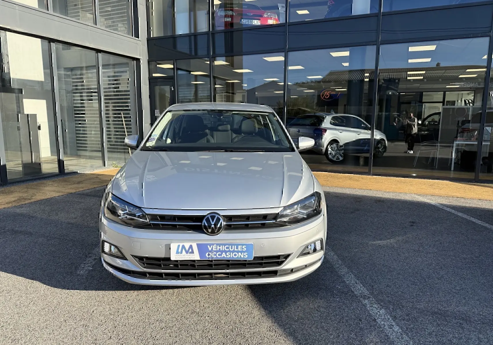 Vue avant d'une Volkswagen Polo gris métal 2021, version 1.0 TSI 95 Lounge Business, devant une vitrine de concession.