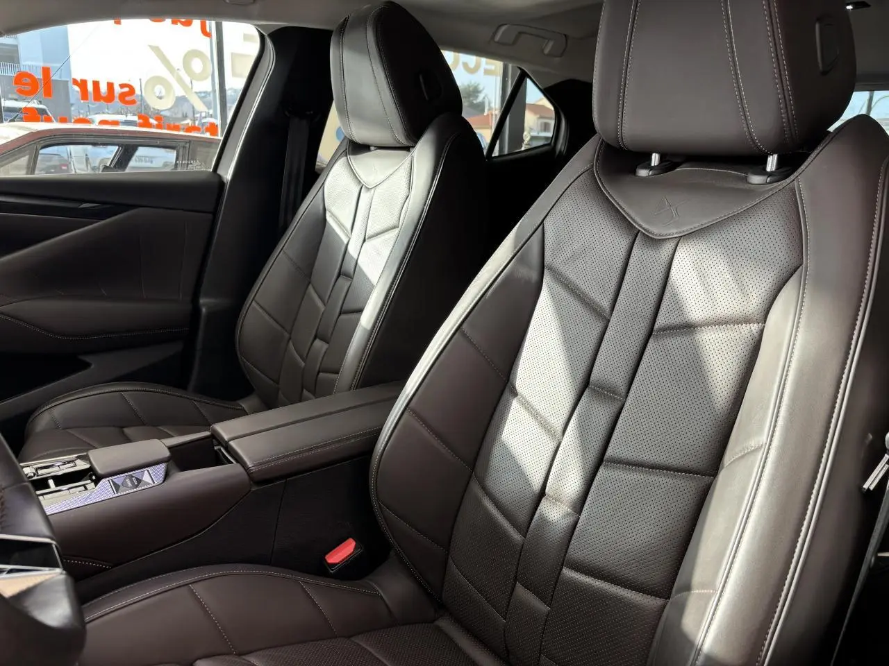 Vue rapprochée des sièges avant en cuir brun Nappa du DS4 E-Tense 2023 avec accoudoir central et surpiqûres visibles.