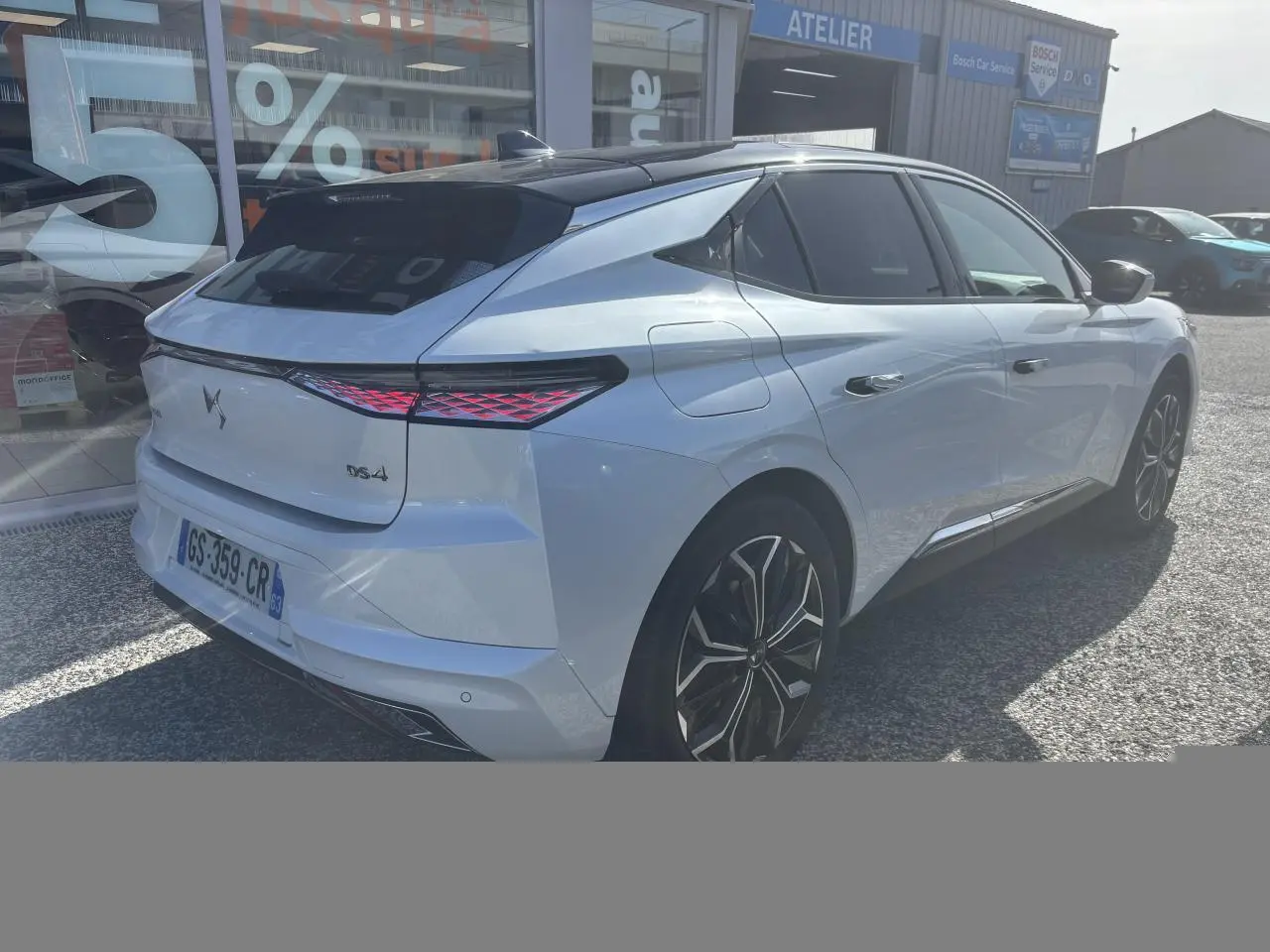 Vue 3/4 arrière droite d'une DS4 blanche avec feux arrière LED et jantes alliage noires devant un atelier Bosch.