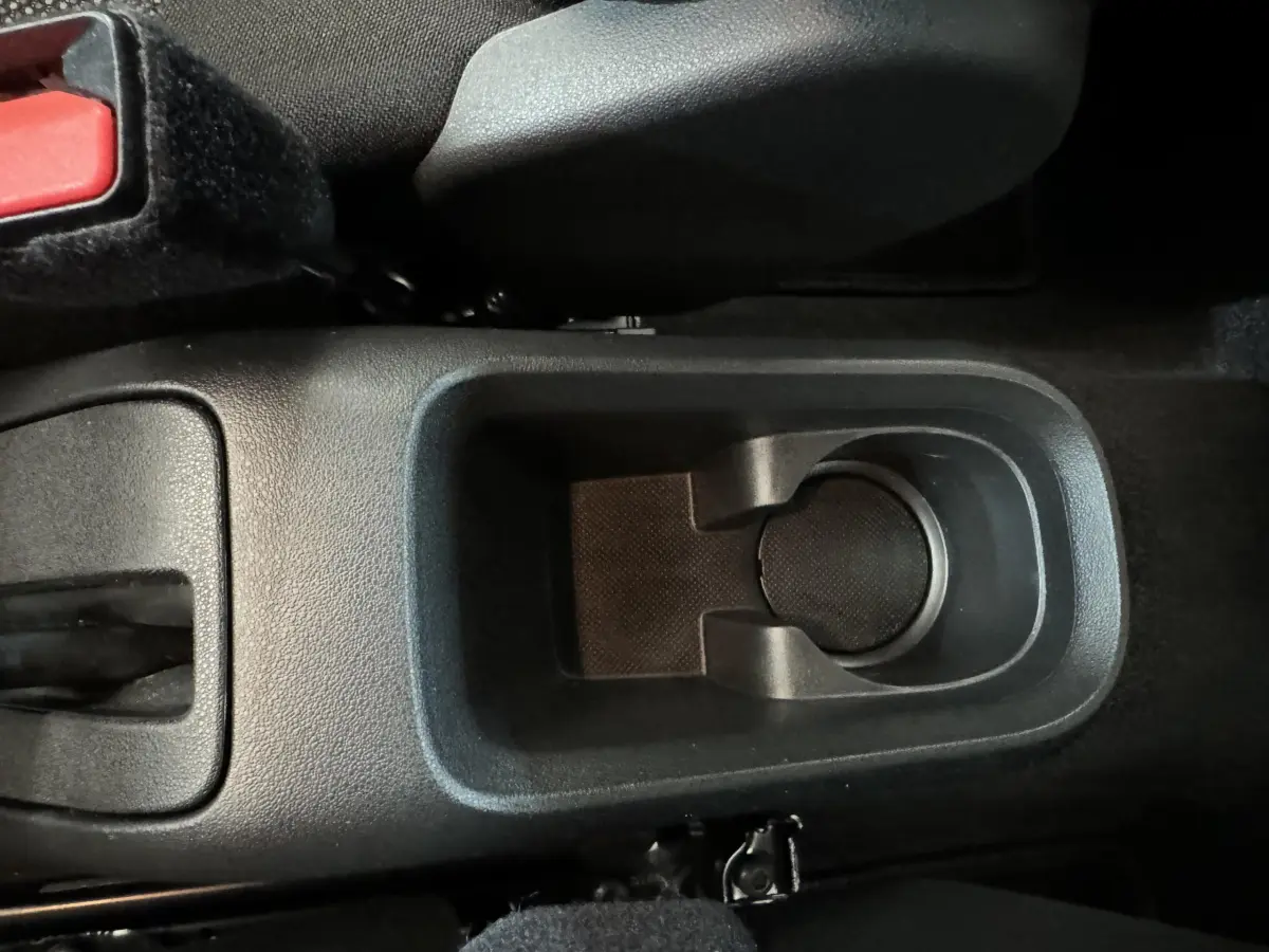 Gros plan sur le porte-gobelet central noir et la console entre les sièges avant d'une Citroën C3 gris foncé.
