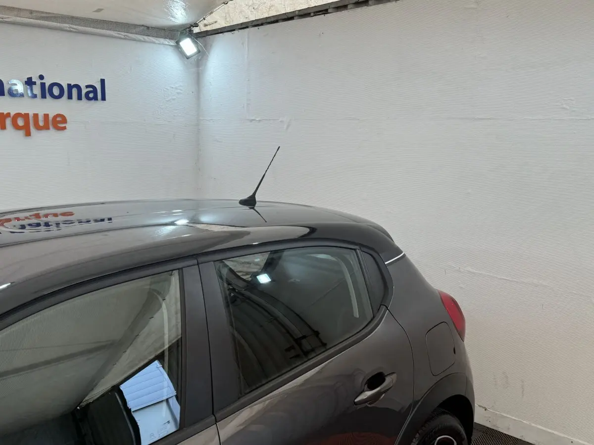 Vue 3/4 arrière droit d'une Citroën C3 gris foncé avec antenne sur le toit dans un garage blanc.