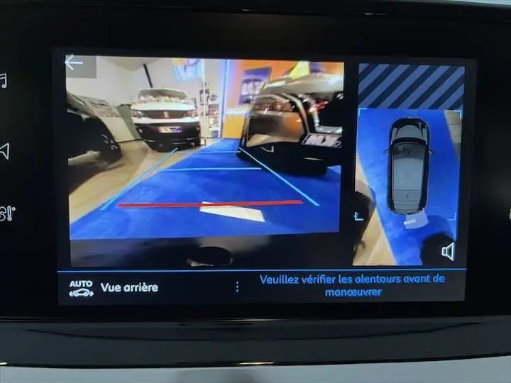 Affichage caméra de recul montrant un parking intérieur avec un véhicule blanc à gauche et un autre noir à droite.