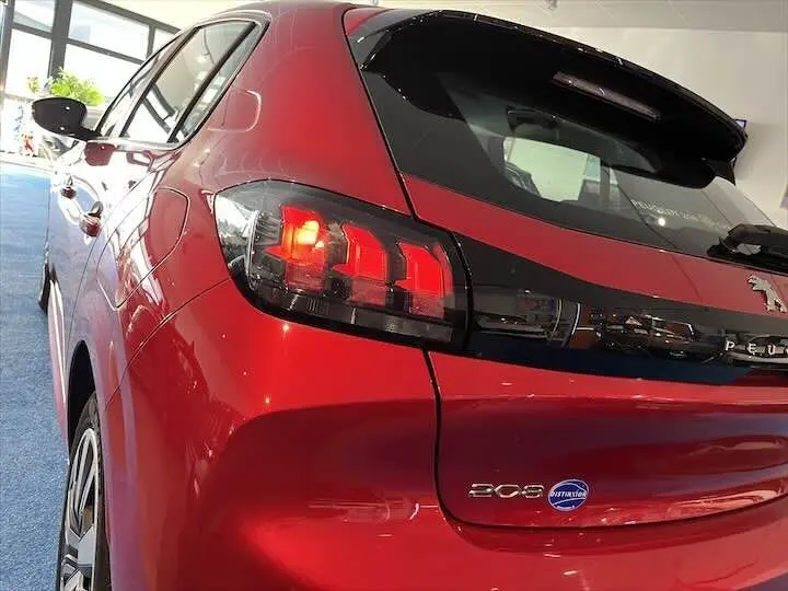 Vue 3/4 arrière gauche d'une Peugeot 208 rouge Elixir Metal avec feux arrière allumés et badge Distinxion visible.