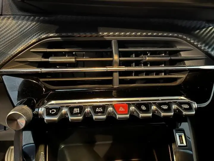 Gros plan sur la console centrale avec les commandes de climatisation et la sortie d'air du Peugeot 208 rouge Elixir Metal.