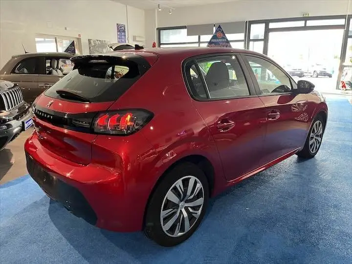 Vue 3/4 arrière droite d'une Peugeot 208 rouge Elixir Metal dans un showroom lumineux.