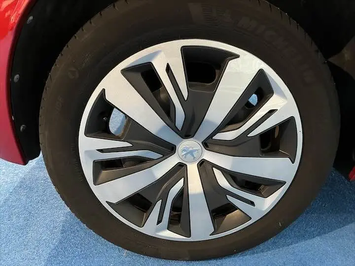 Gros plan sur la roue avant gauche d'une Peugeot 208 rouge Elixir Metal avec jante alliage au design moderne noir et argent.