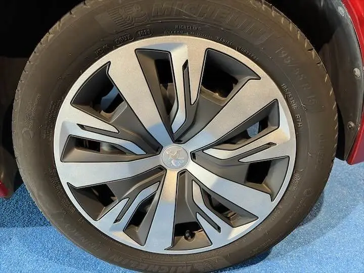 Gros plan sur la roue avant droite d'une Peugeot 208 rouge Elixir Metal avec jante alliage au design moderne.