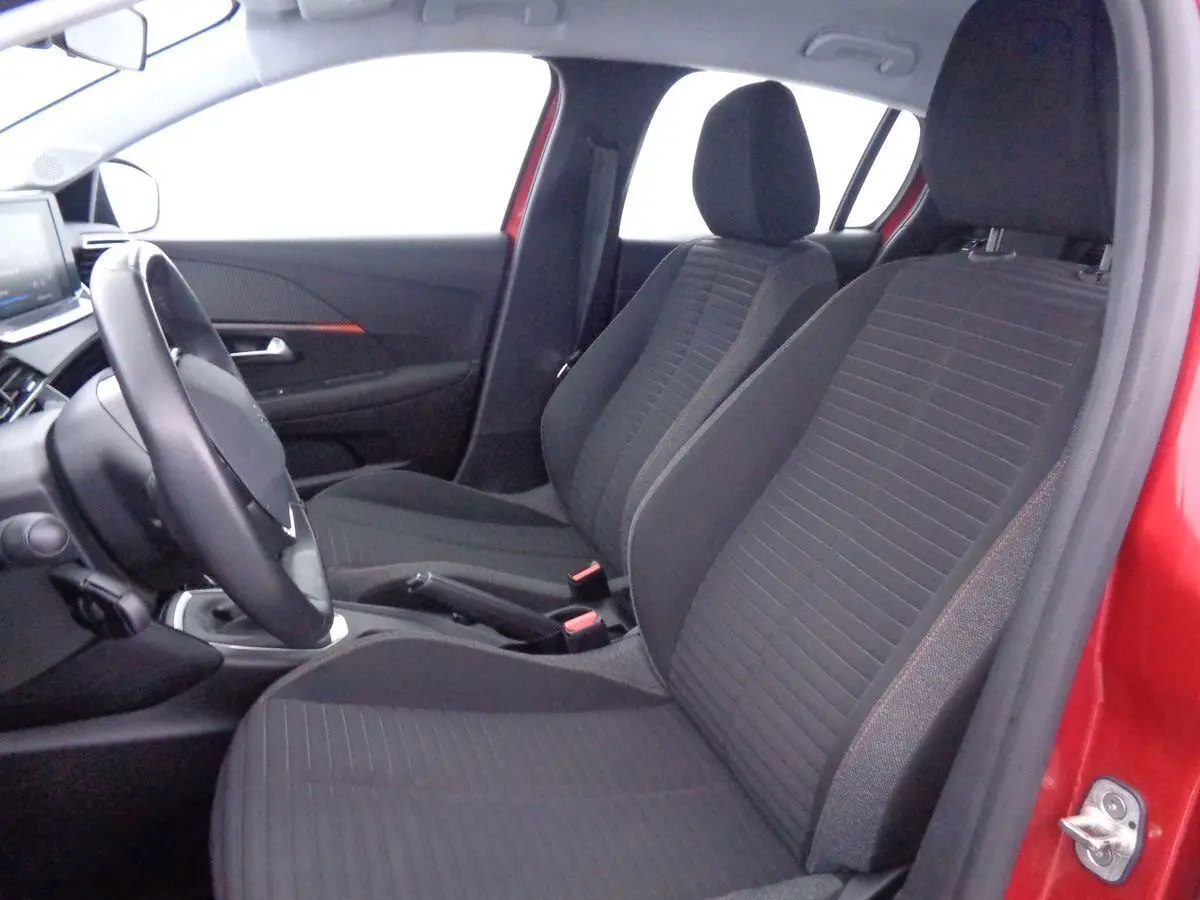 Intérieur avant droit de la Peugeot 208 rouge Elixir Metal, montrant les sièges tissu gris et le volant.