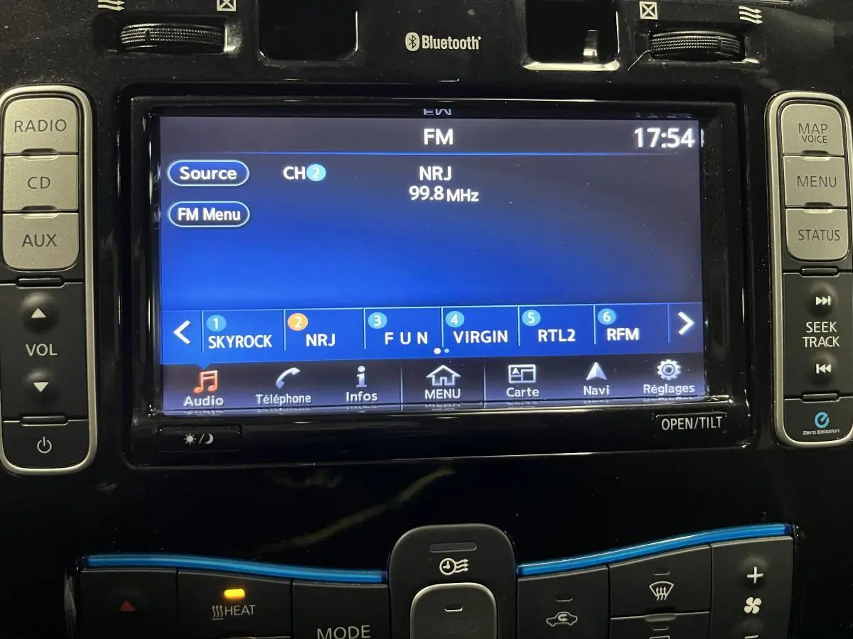 Gros plan sur l'écran tactile central et commandes audio d'une Nissan Leaf rouge de 2017, affichant la radio FM NRJ.
