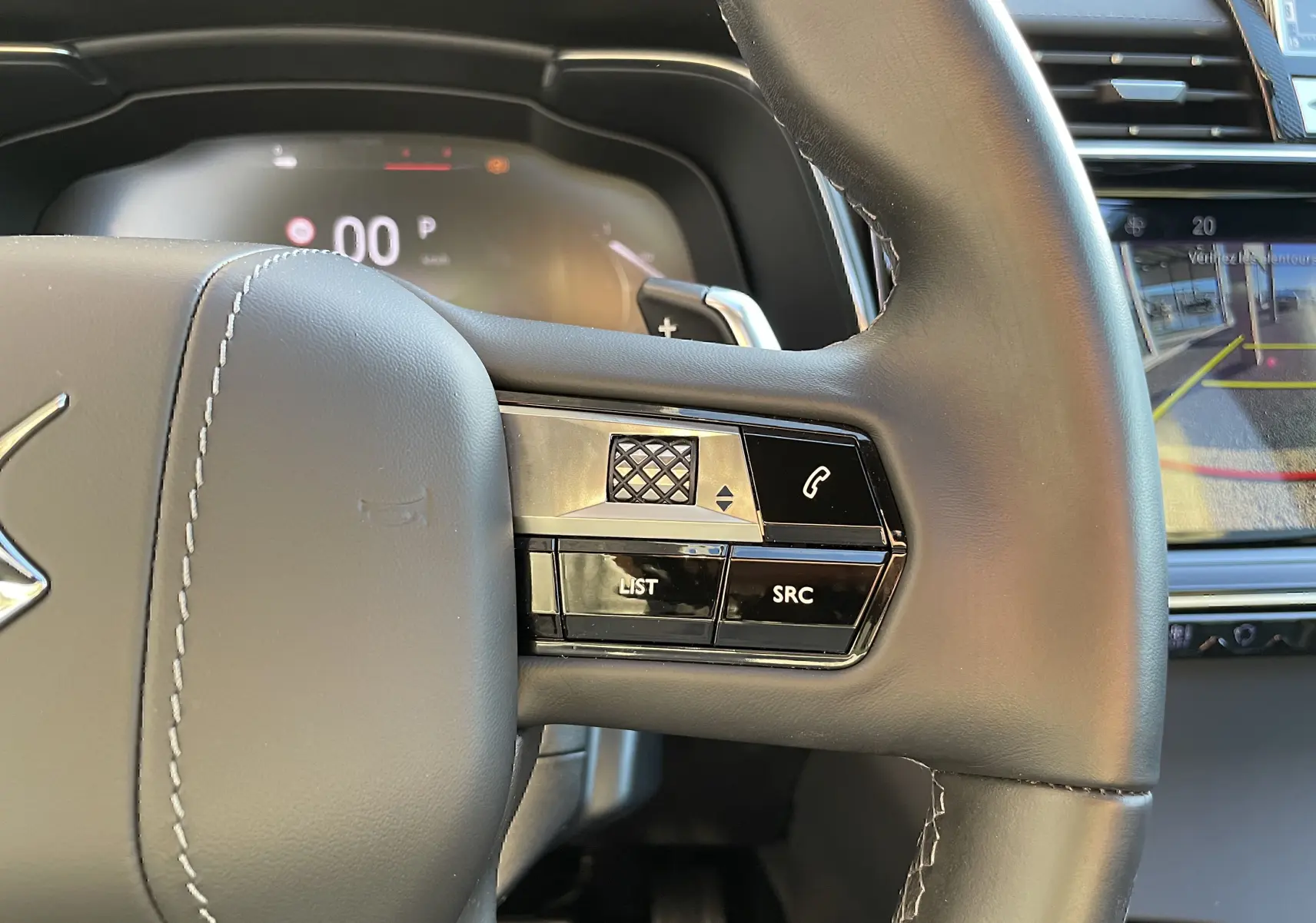 Gros plan sur le côté droit du volant en cuir noir du DS7 2024 avec commandes audio et écran de caméra de recul visible.