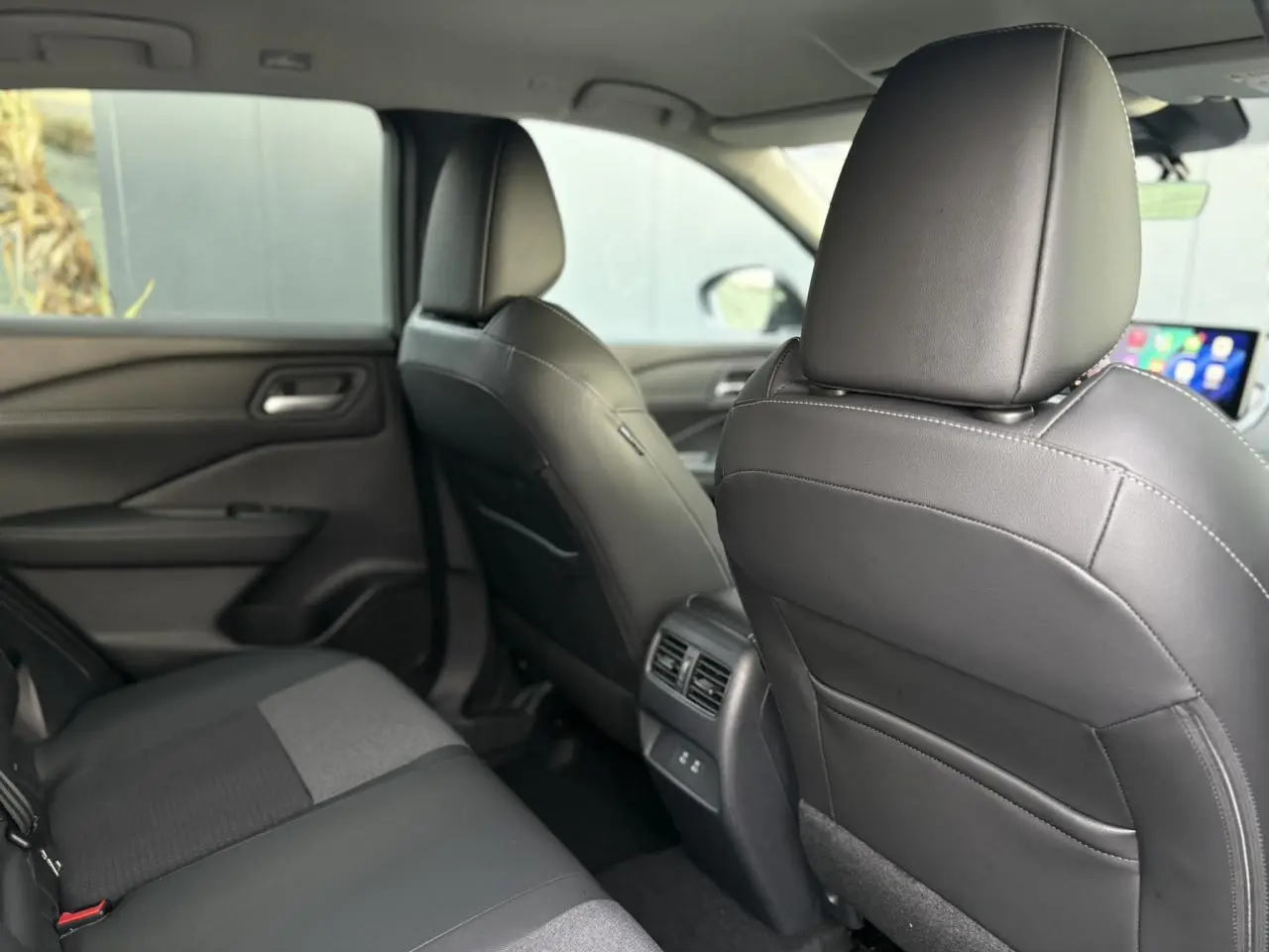 Vue intérieure arrière du Nissan Qashqai III gris Ceramic, sièges en cuir noir et tissu, avec aérateurs centraux et ports USB.
