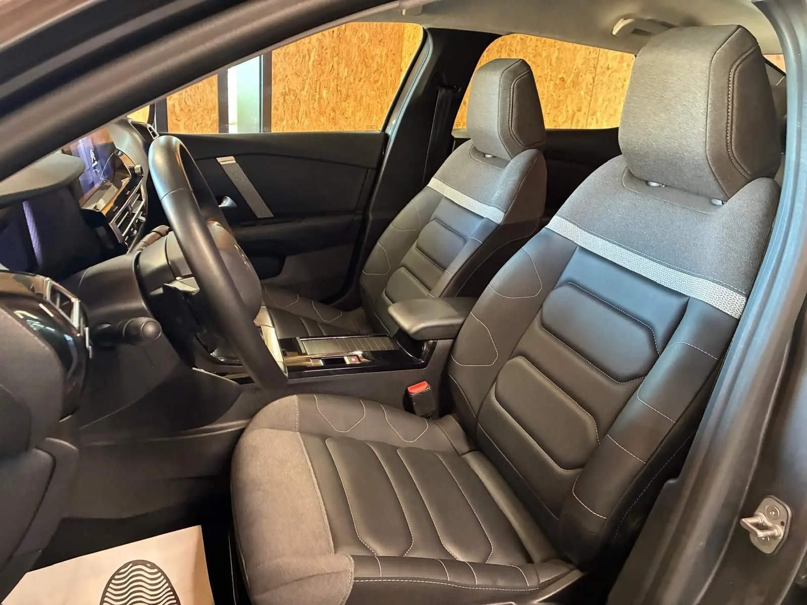 Vue intérieure côté conducteur du Citroën C4 X 2024, sièges tissu gris et cuir noir avec console centrale moderne.