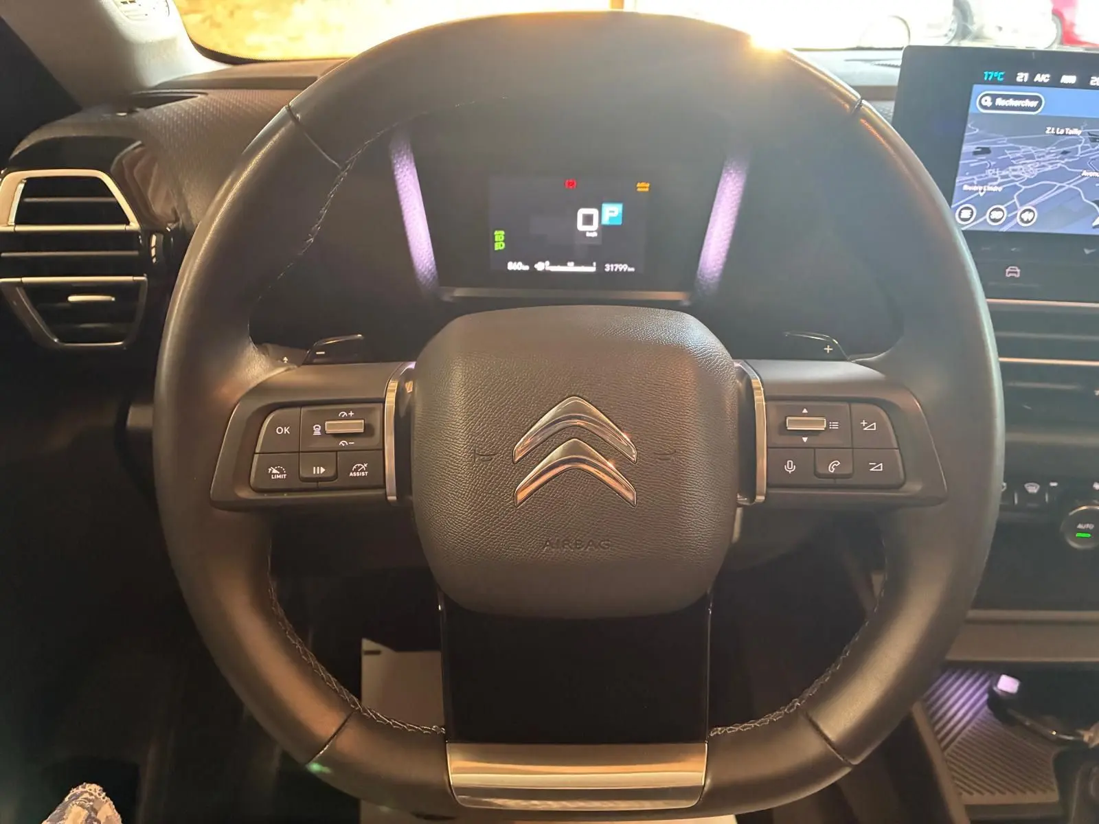 Vue rapprochée du volant en cuir noir du Citroën C4 X 2024, avec commandes intégrées et tableau de bord numérique allumé.