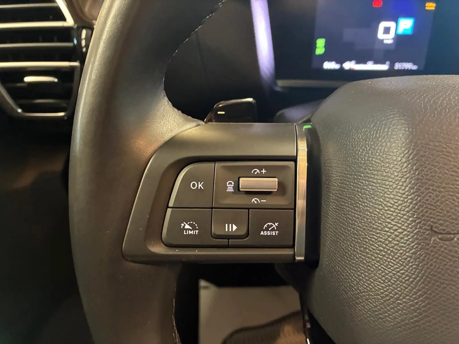 Gros plan sur les commandes à gauche du volant noir du Citroën C4 X 2024, avec affichage numérique en arrière-plan.