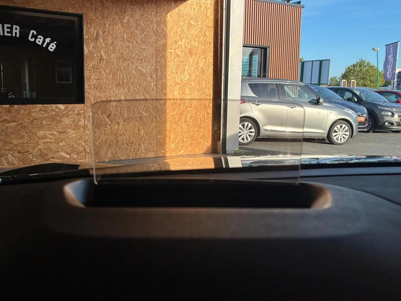 Vue depuis l'intérieur sur le tableau de bord avec tête haute, montrant une Citroën C4 X gris métallisé en stationnement côté droit.