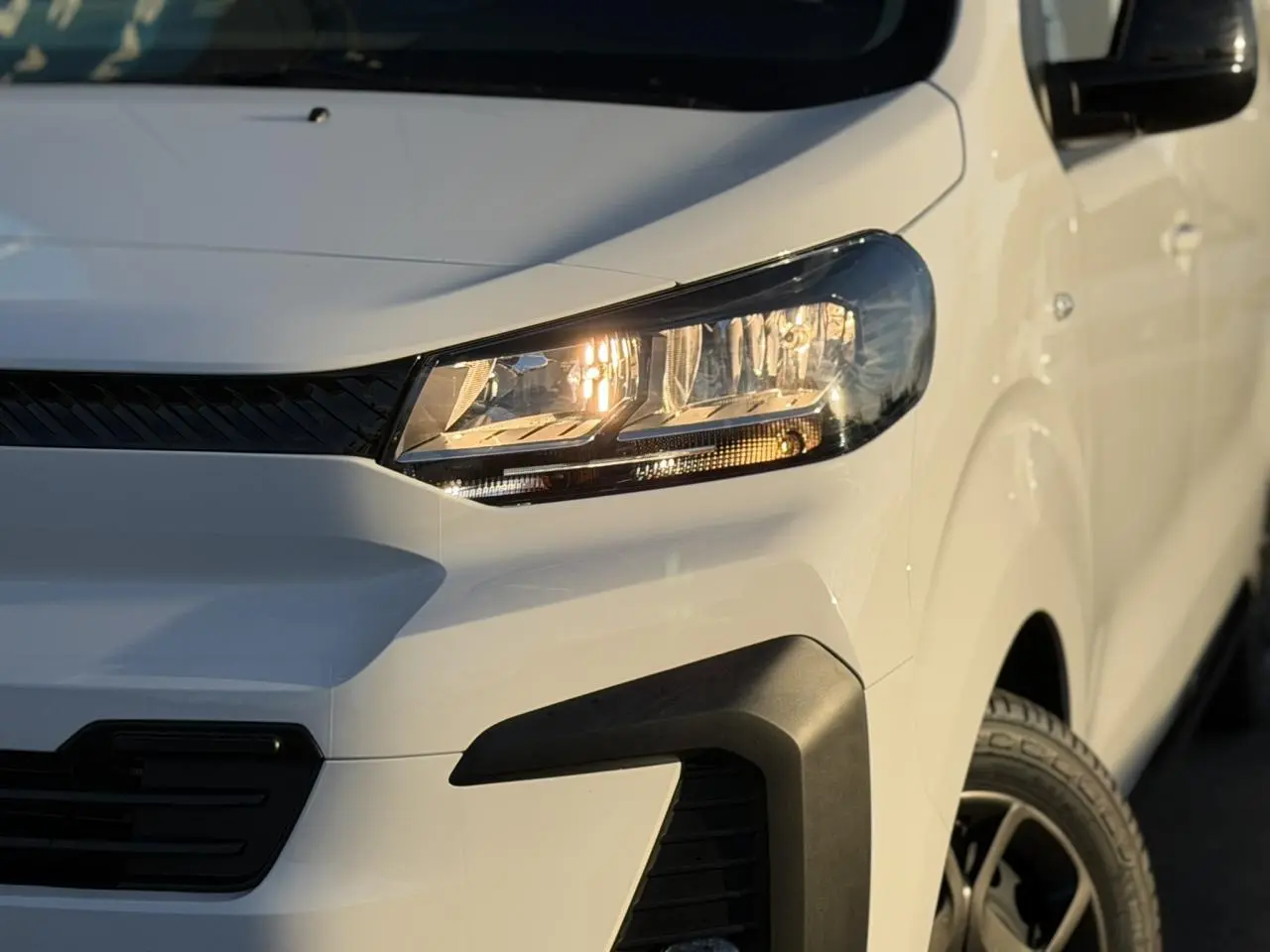Gros plan sur l'avant droit du Citroën Jumpy XL blanc Icy avec phares allumés et bouclier noir du Pack Look.