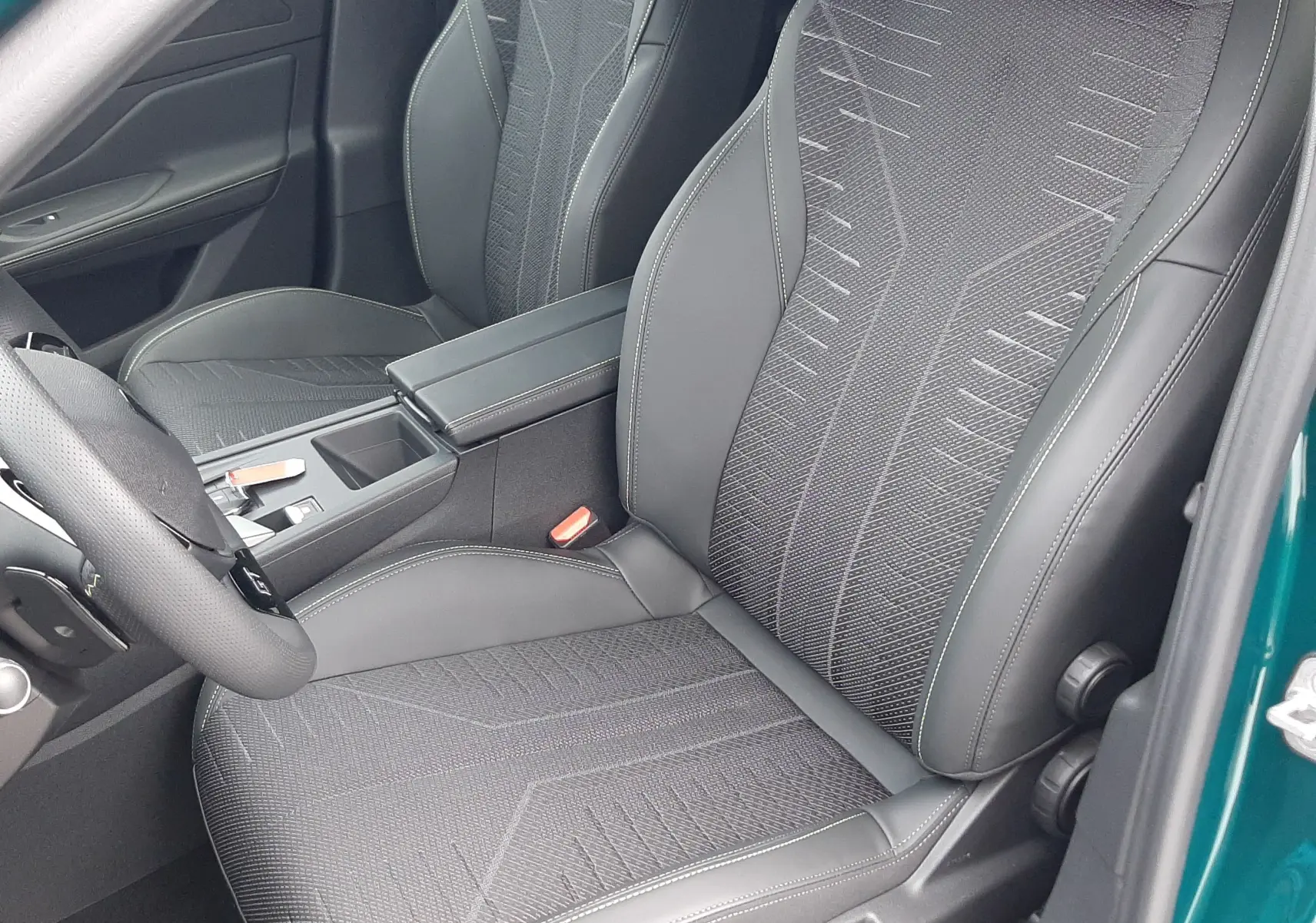 Vue intérieure côté conducteur de la Peugeot 308 2025 bleu Lagoa, sièges noirs avec surpiqûres et console centrale visible.