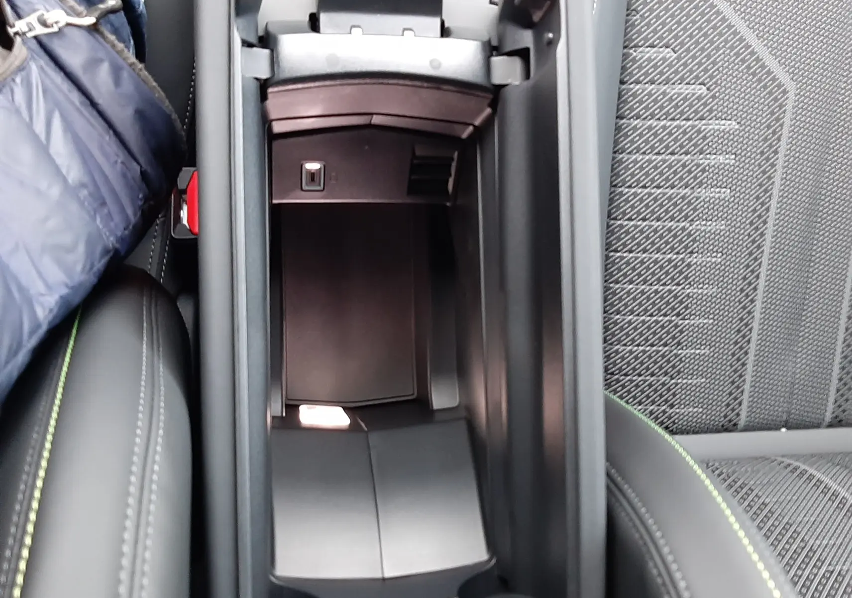 Vue plongeante sur le rangement central ouvert de la Peugeot 308 2025, intérieur noir avec surpiqûres vertes visibles.