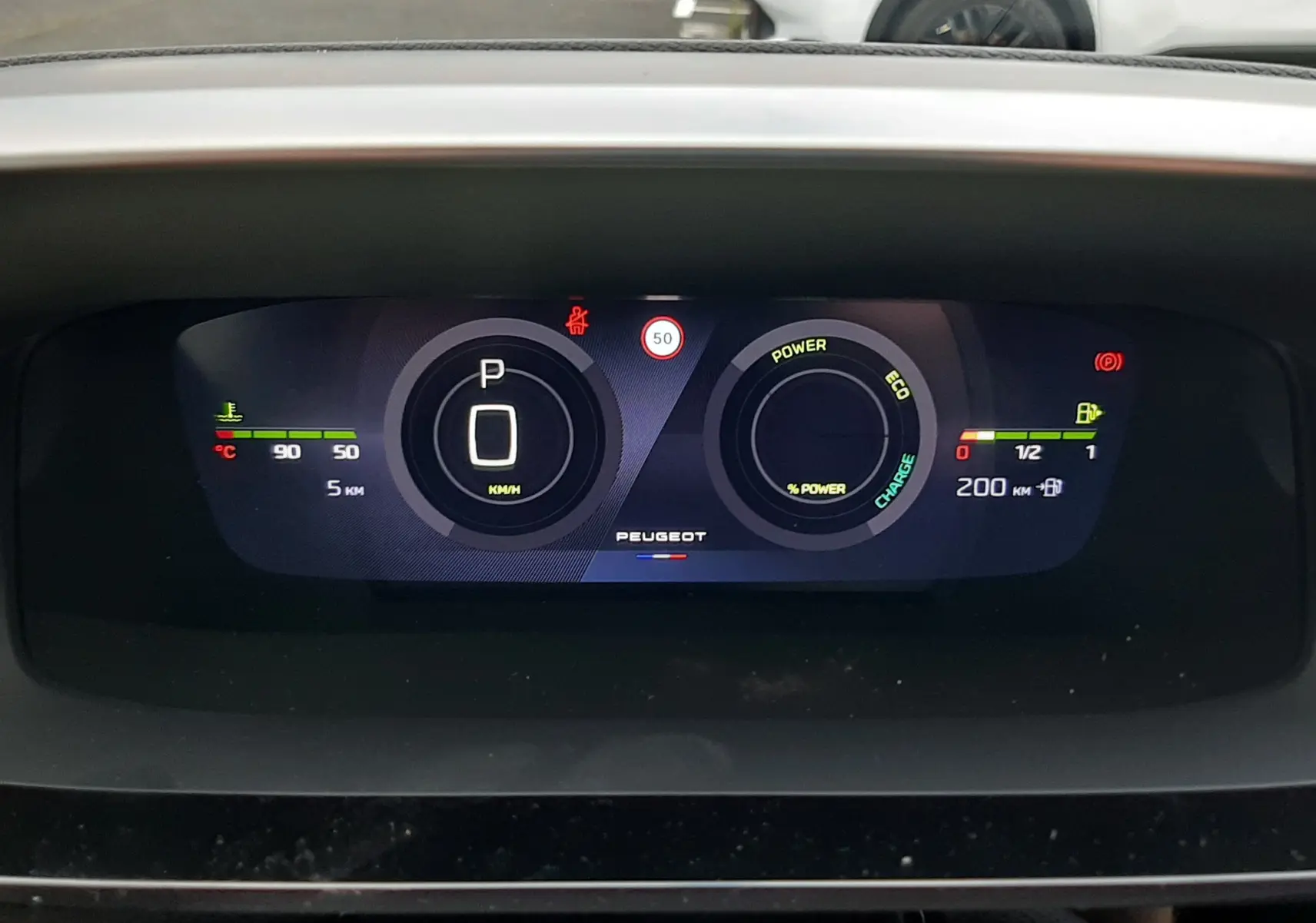 Tableau de bord numérique de Peugeot 308 hybride 2025 affichant vitesse à zéro et indicateurs de puissance et autonomie.