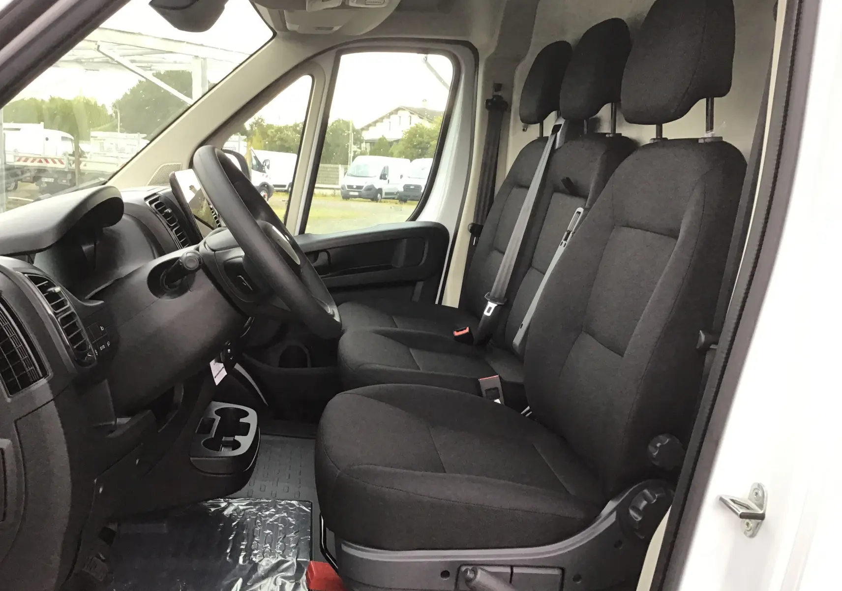 Intérieur du Peugeot Boxer Fourgon blanc 2025, vue côté conducteur sur les trois sièges noirs et le tableau de bord.