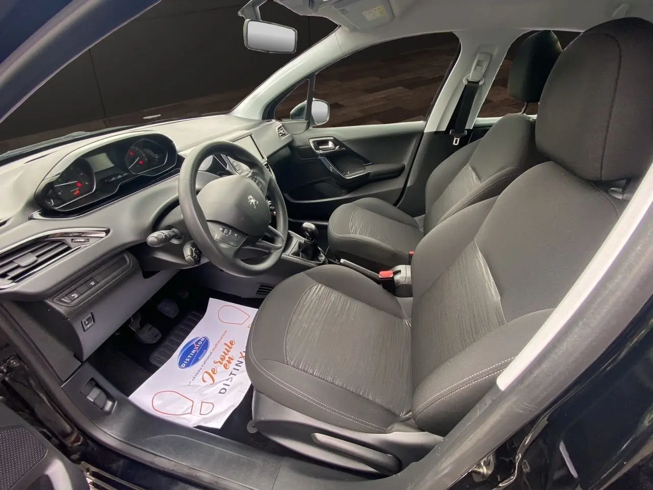 Intérieur avant droit d'une Peugeot 208 Affaire noire 2019, sièges tissu noir et tableau de bord avec volant compact.