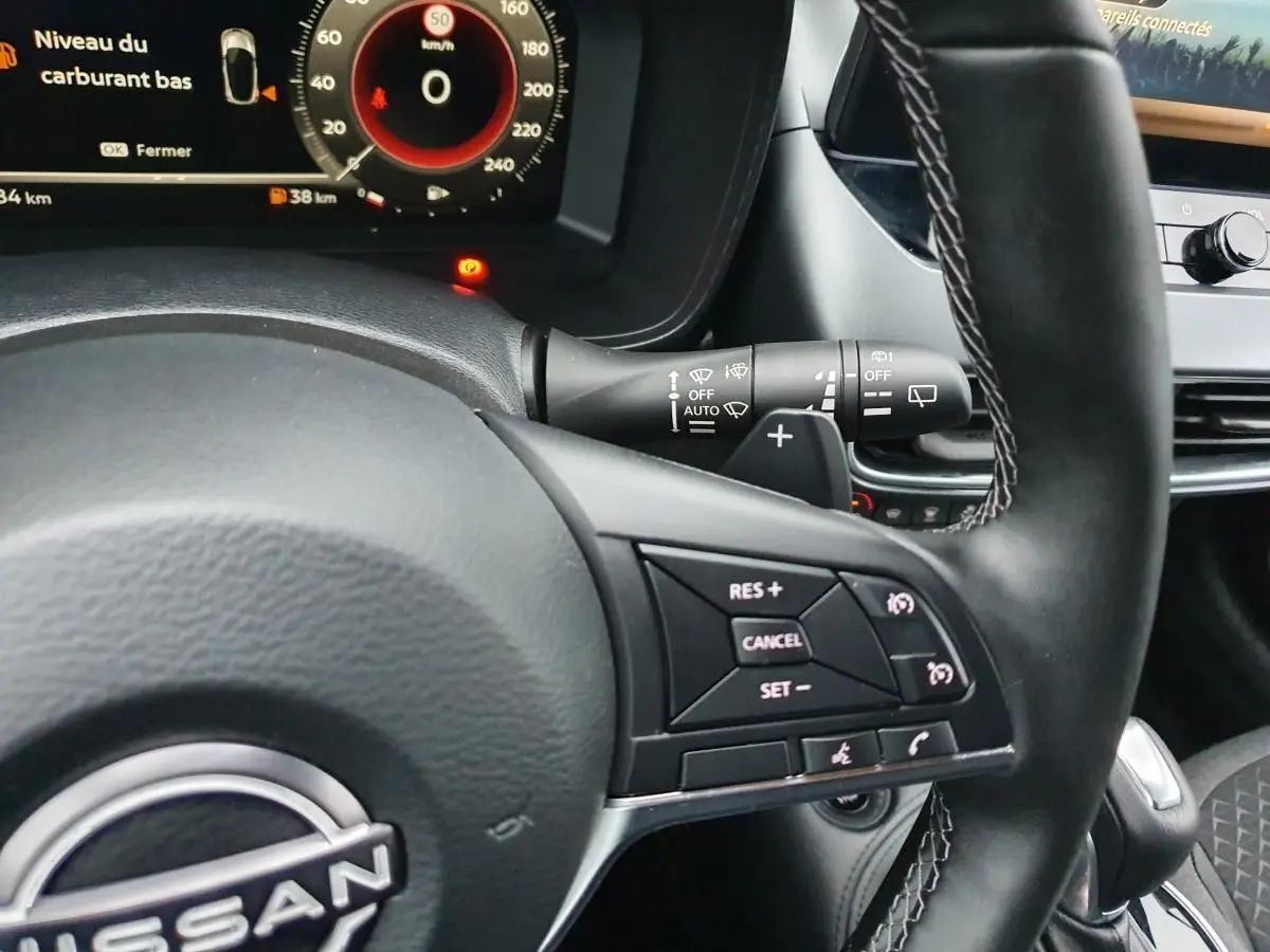 Vue rapprochée du volant noir du Nissan Juke 2025 avec commandes de régulateur et tableau de bord numérique.