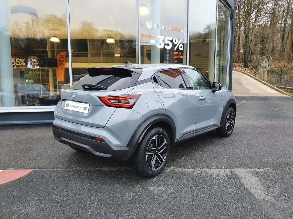 Nissan Juke gris céramique vu en 3/4 arrière droit, avec jantes alliage 17'' et antenne aileron de requin noire.