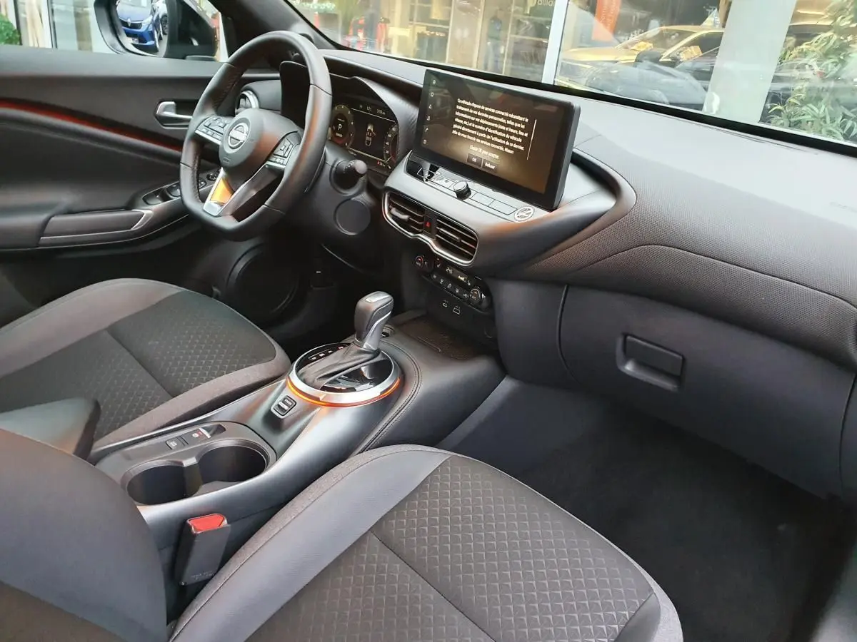 Intérieur du Nissan Juke 2025 en gris céramique, vue côté conducteur sur tableau de bord et console centrale avec écran tactile.