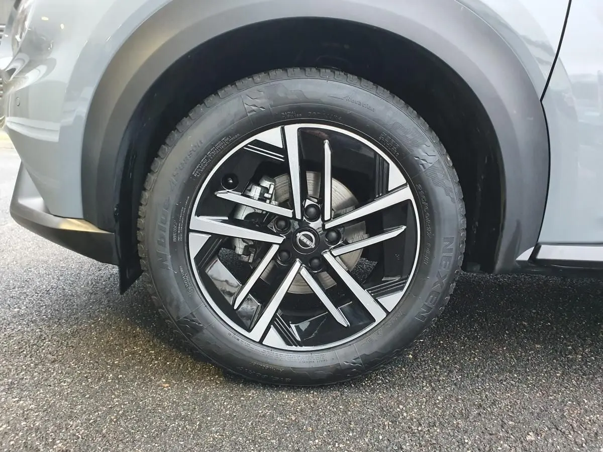 Gros plan sur la roue avant gauche du Nissan Juke gris céramique avec jante alliage noire et argentée.