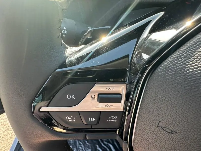 Gros plan sur les commandes au volant noir brillant de la Peugeot 308 bleu, avec boutons de régulateur et assistant de conduite.