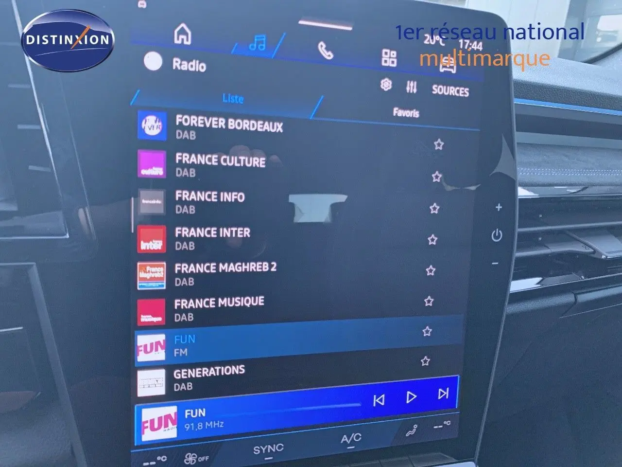 Écran tactile central du tableau de bord du Renault Austral blanc métal avec toit noir, affichant les stations radio numériques.