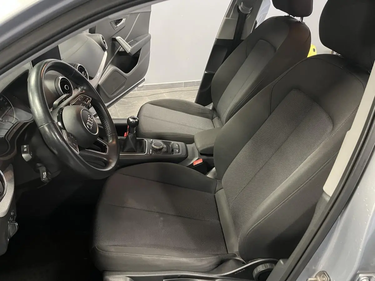Intérieur avant droit de l'Audi Q2 gris 2019 avec sièges en tissu noir et volant multifonction en cuir.