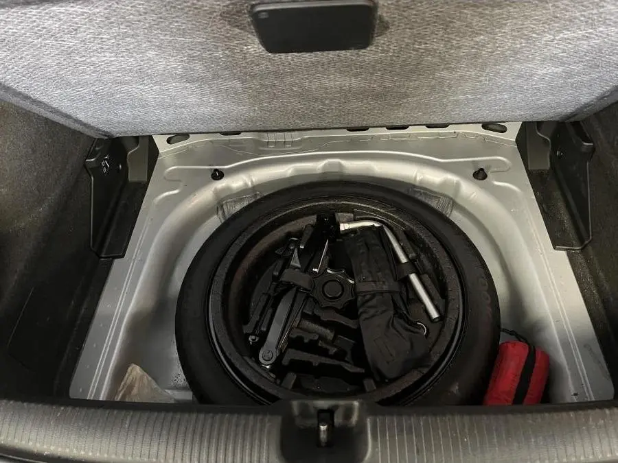 Vue du coffre ouvert de l'Audi Q2 gris montrant la roue de secours compacte et les outils de dépannage rangés.