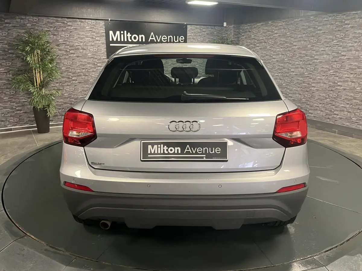 Vue arrière d'un Audi Q2 gris métallisé avec feux arrière rouges et pare-chocs inférieur noir dans un showroom.