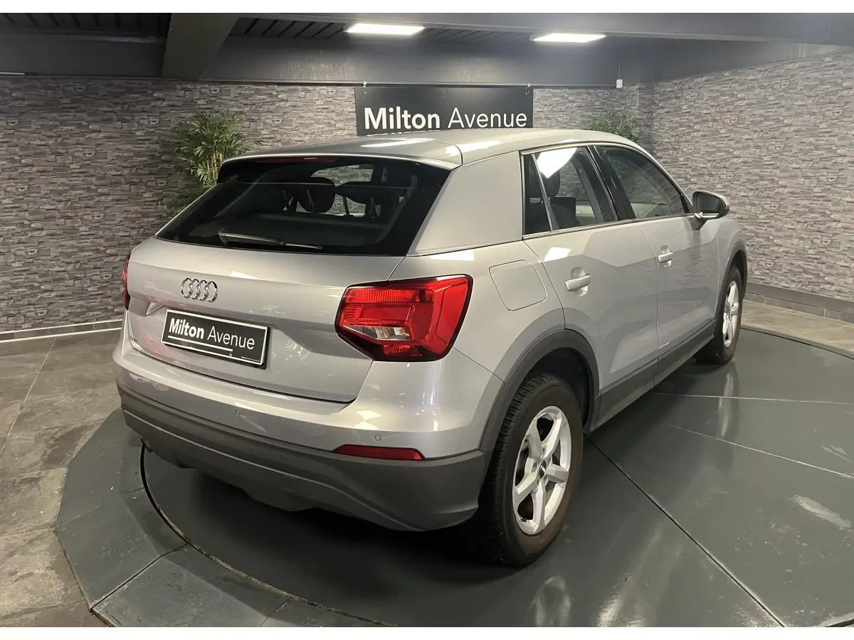 Audi Q2 gris vue 3/4 arrière droit, avec feux arrière rouges et jantes 16 pouces cinq branches.