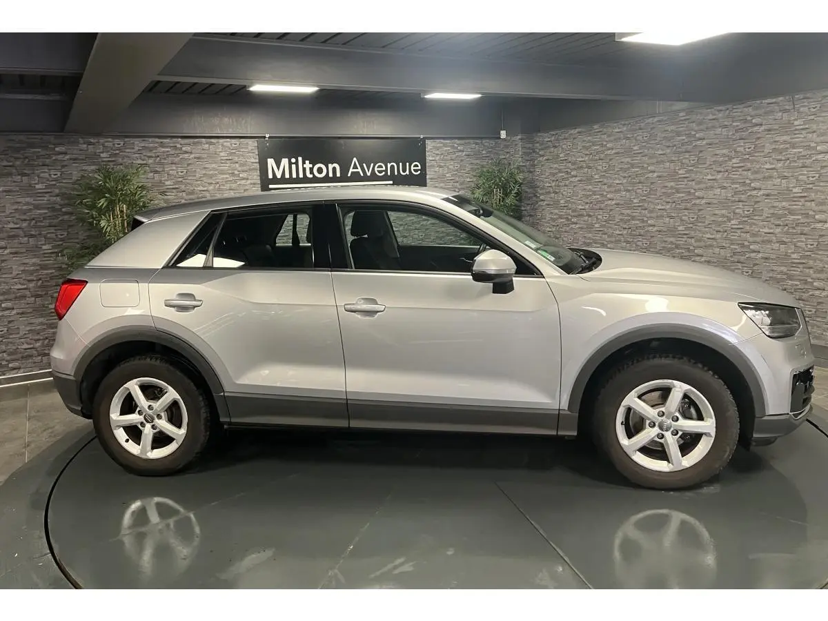 Audi Q2 gris vue de profil côté gauche dans un showroom avec jantes 5 branches et protections noires sur les bas de caisse.