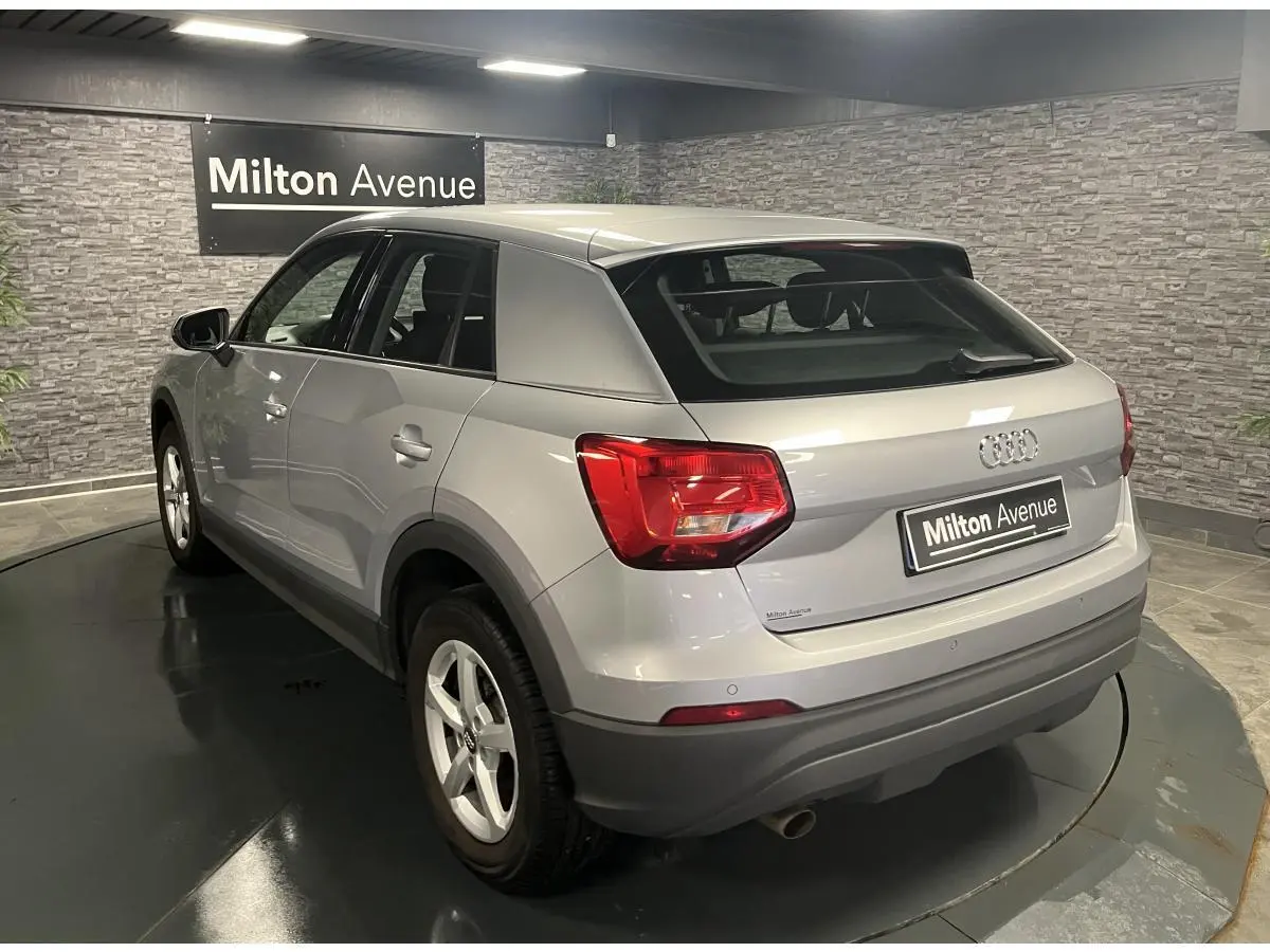 Audi Q2 gris métallisé vue 3/4 arrière droit, avec feux arrière rouges et jantes 16 pouces cinq branches.