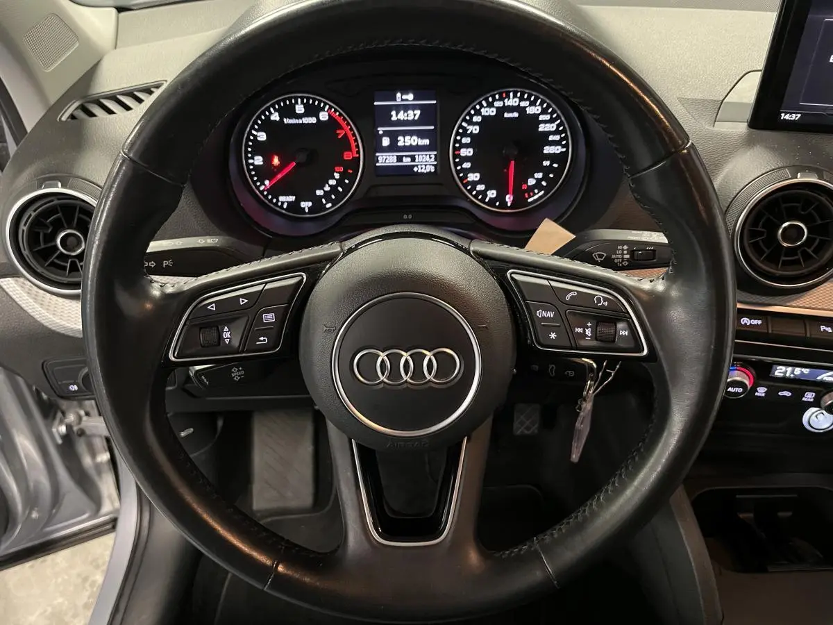 Vue intérieure centrée sur le volant cuir multifonction et la console centrale d'une Audi Q2 Business line gris 2019.