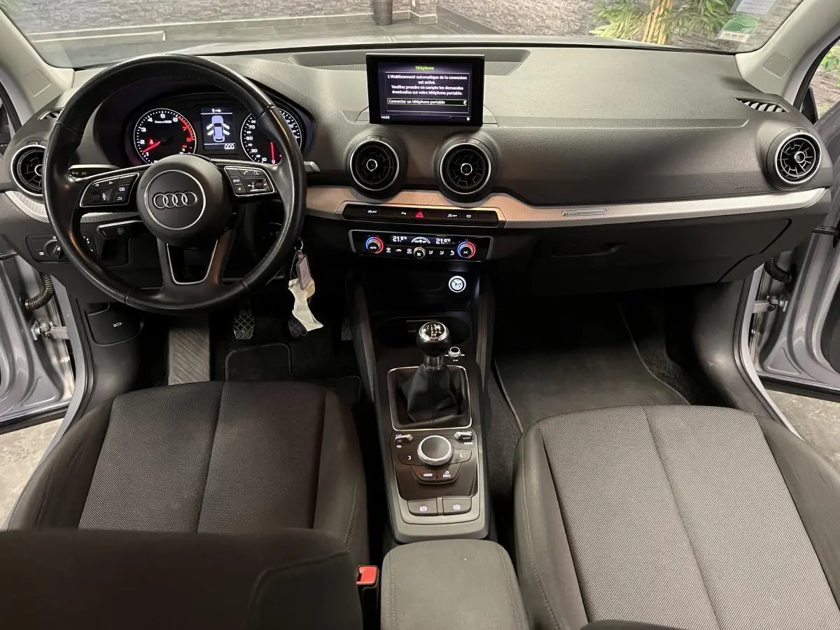 Intérieur Audi Q2 Business line 2019 vu de face, volant cuir, tableau de bord noir et console centrale avec boîte manuelle.