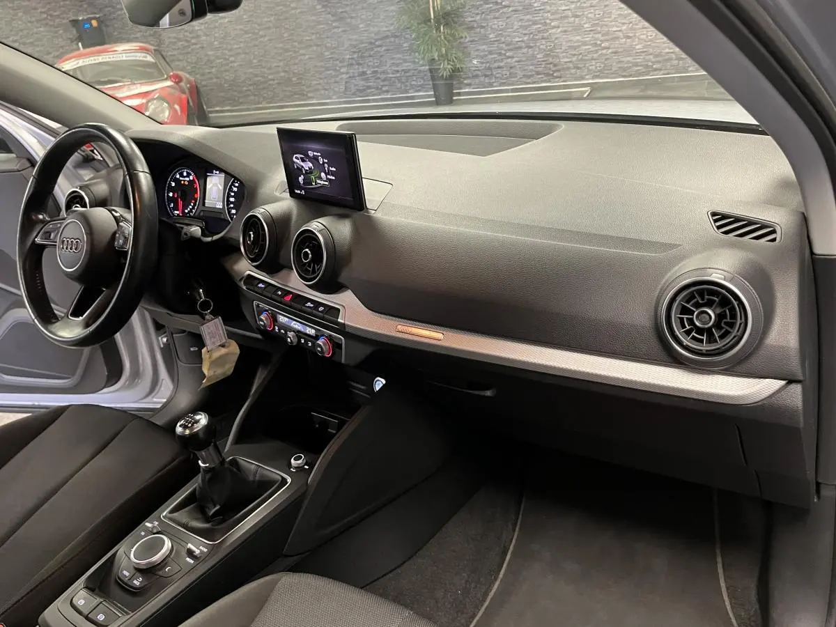 Intérieur avant droit de l'Audi Q2 gris, tableau de bord noir avec écran central et levier de vitesses manuel.