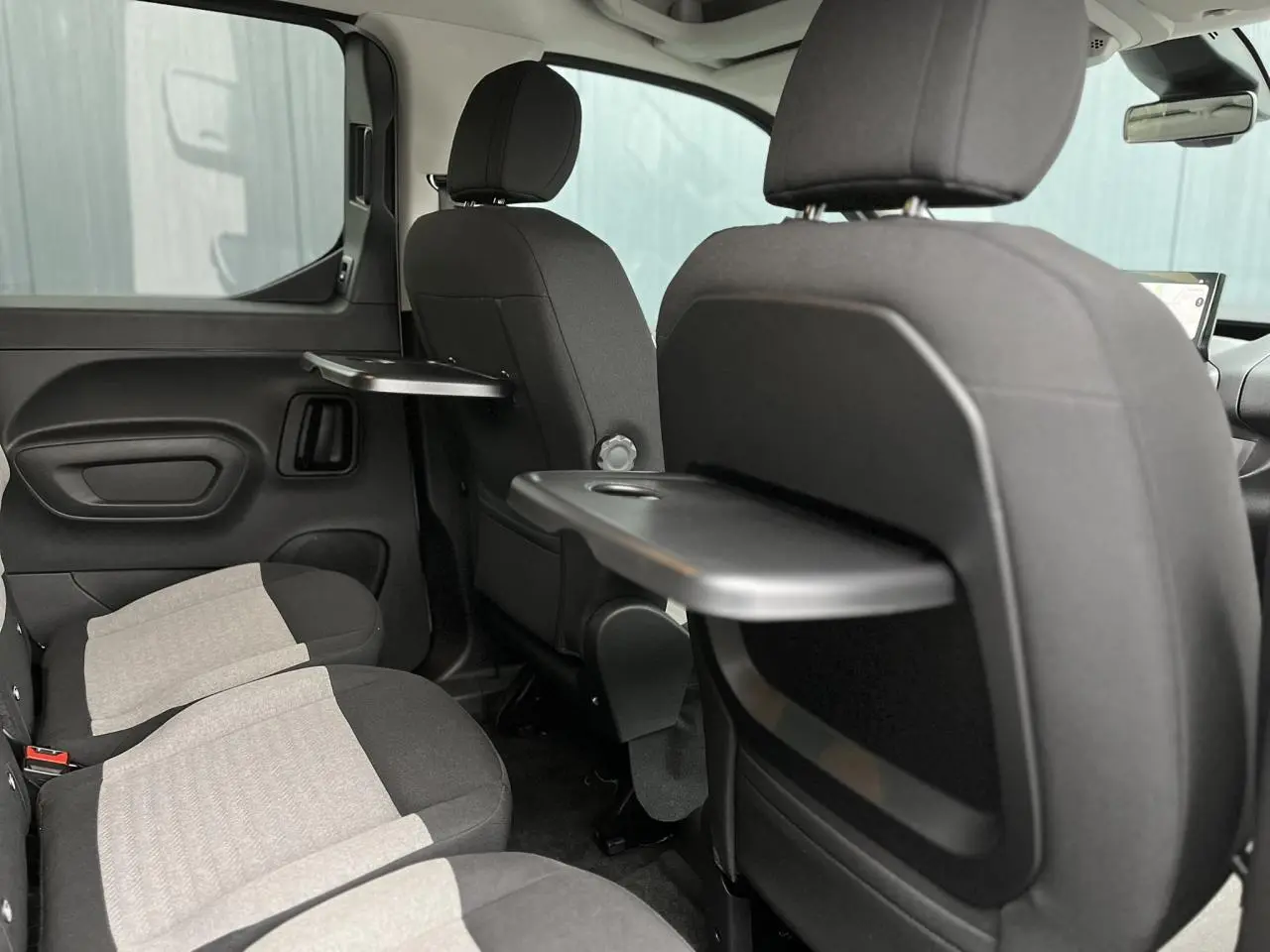Vue intérieure arrière droite du Citroën Berlingo Multispace 2025 avec sièges gris et tablettes pliantes noires.