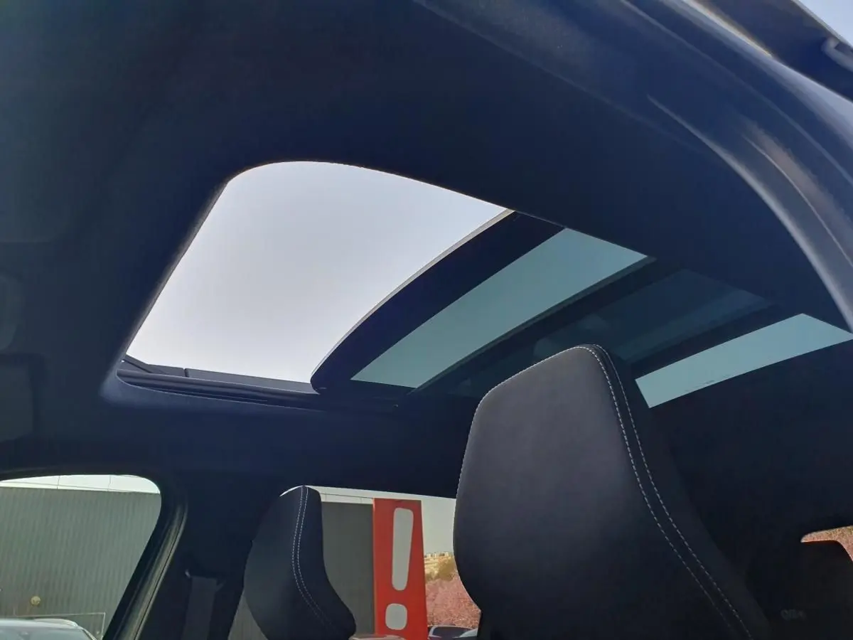 Vue intérieure du toit panoramique ouvert du Dacia Bigster gris schiste, avec appuie-tête avant en tissu noir.