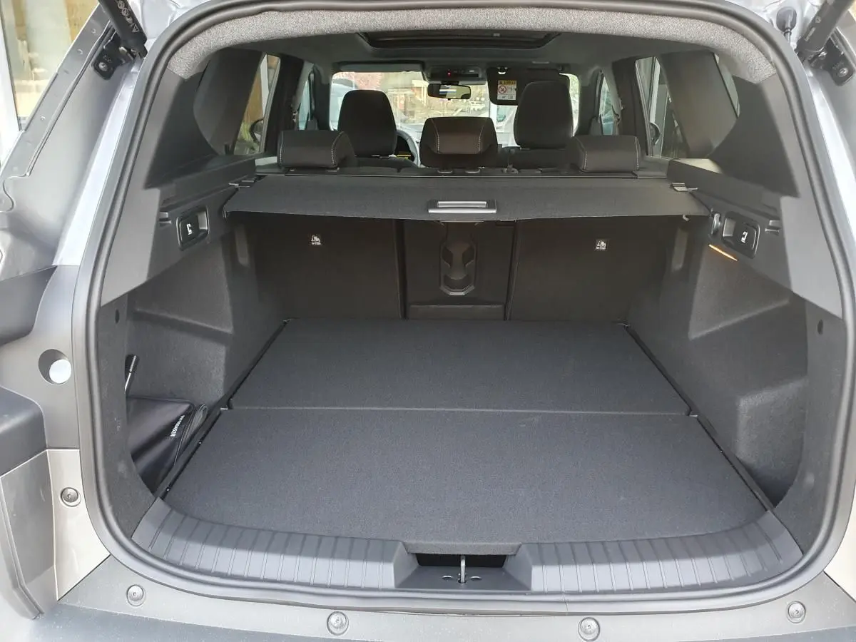 Coffre ouvert vu de l'arrière du Dacia Bigster gris schiste avec cache-bagages et banquette arrière rabattue.