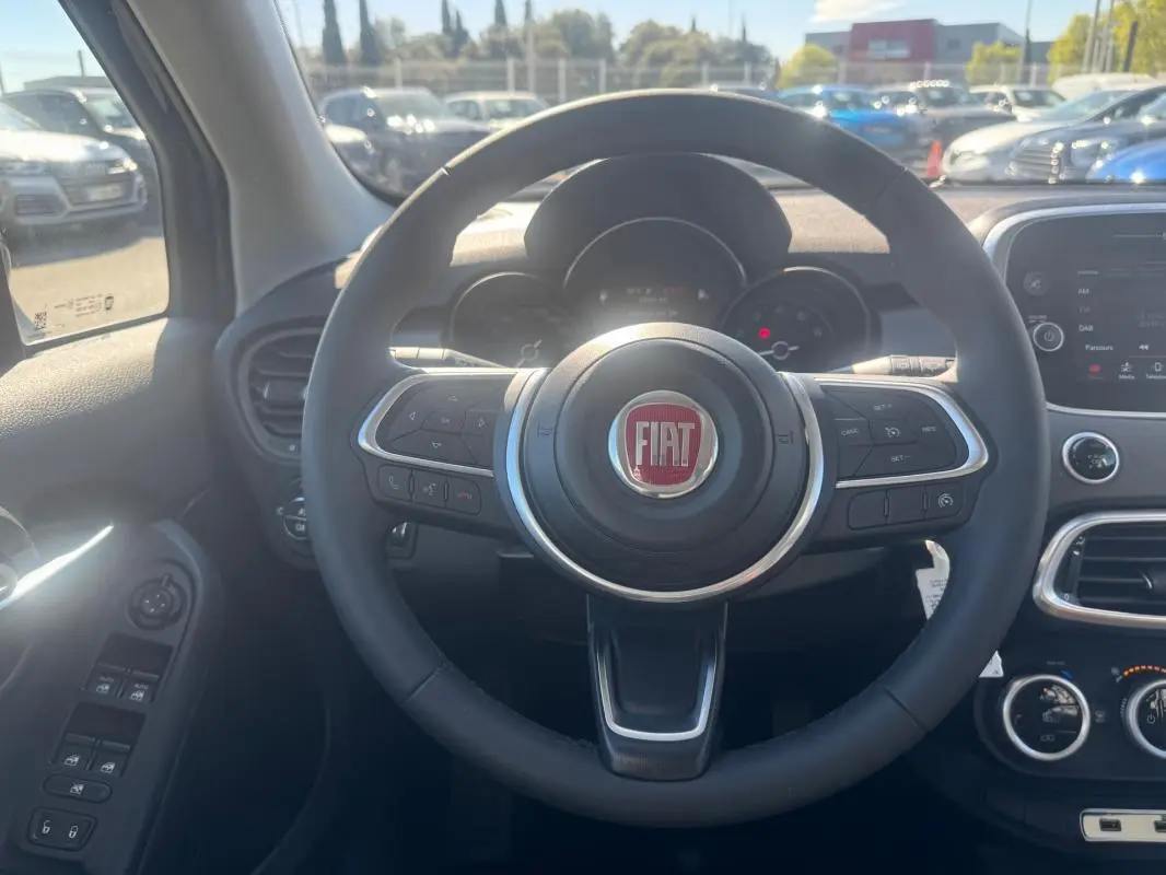 Vue intérieure centrée sur le volant du Fiat 500X MY23 avec tableau de bord et commandes visibles.