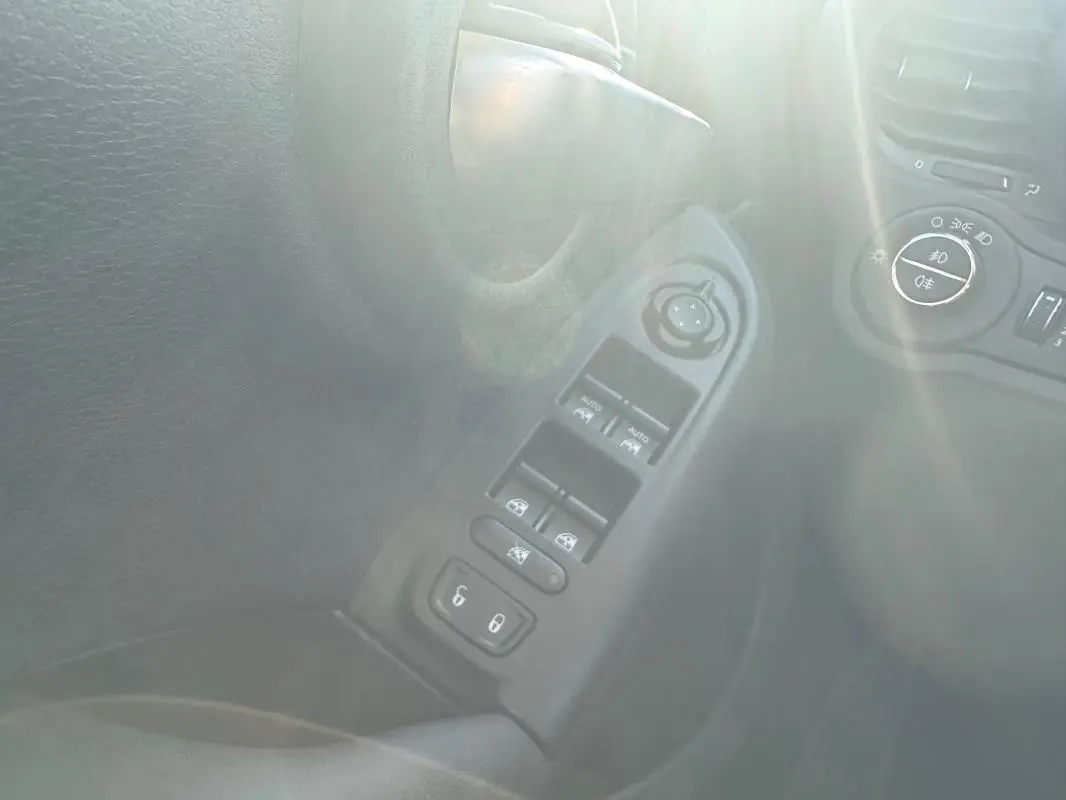 Vue rapprochée du panneau de commandes des vitres électriques et rétroviseurs du côté gauche d’un Fiat 500X bleu MY23.