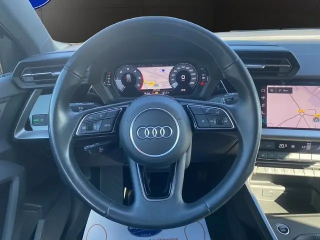 Vue centrée sur le volant cuir noir d'une Audi A3 Sportback 2021 avec tableau de bord digital et écran tactile navigation.