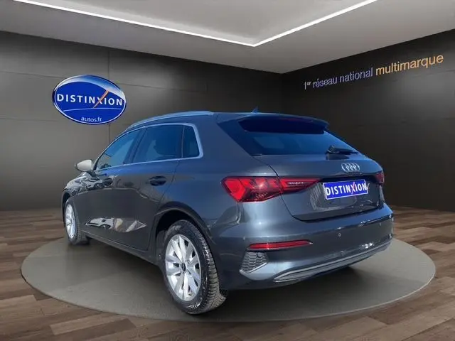 Audi A3 Sportback gris Manhattan vu en 3/4 arrière droit avec vitres arrière surteintées dans un showroom