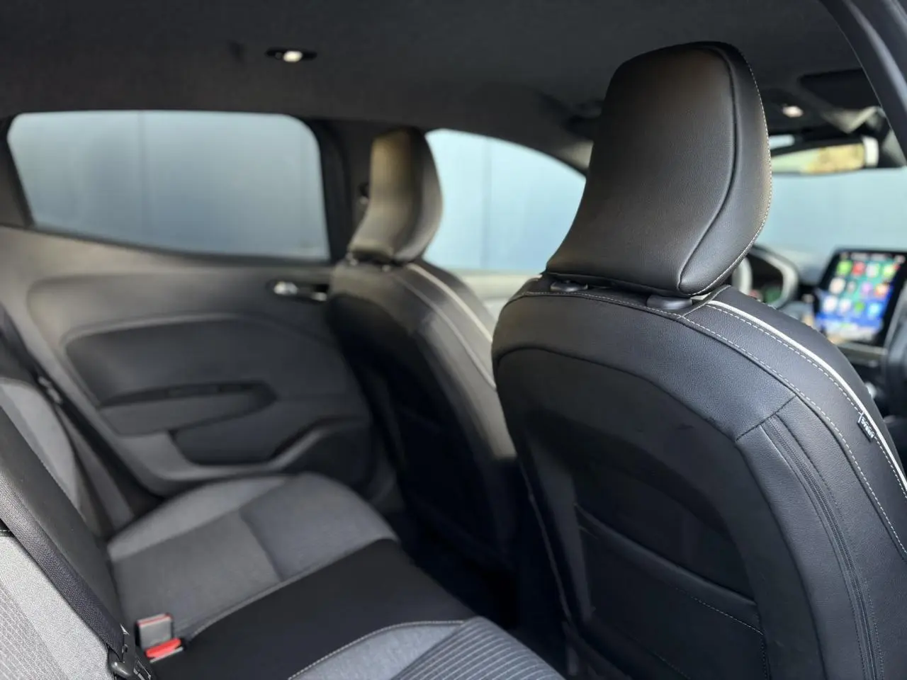 Vue intérieure arrière de la Renault Clio 2025 gris schiste, sièges tissu et cuir noir avec surpiqûres blanches visibles.