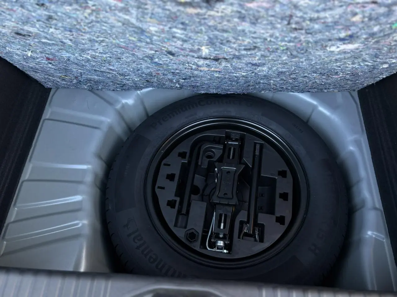 Vue en plongée sur la roue de secours tôle noire et ses outils dans le coffre d'une Renault Clio Gris Schiste 2025.