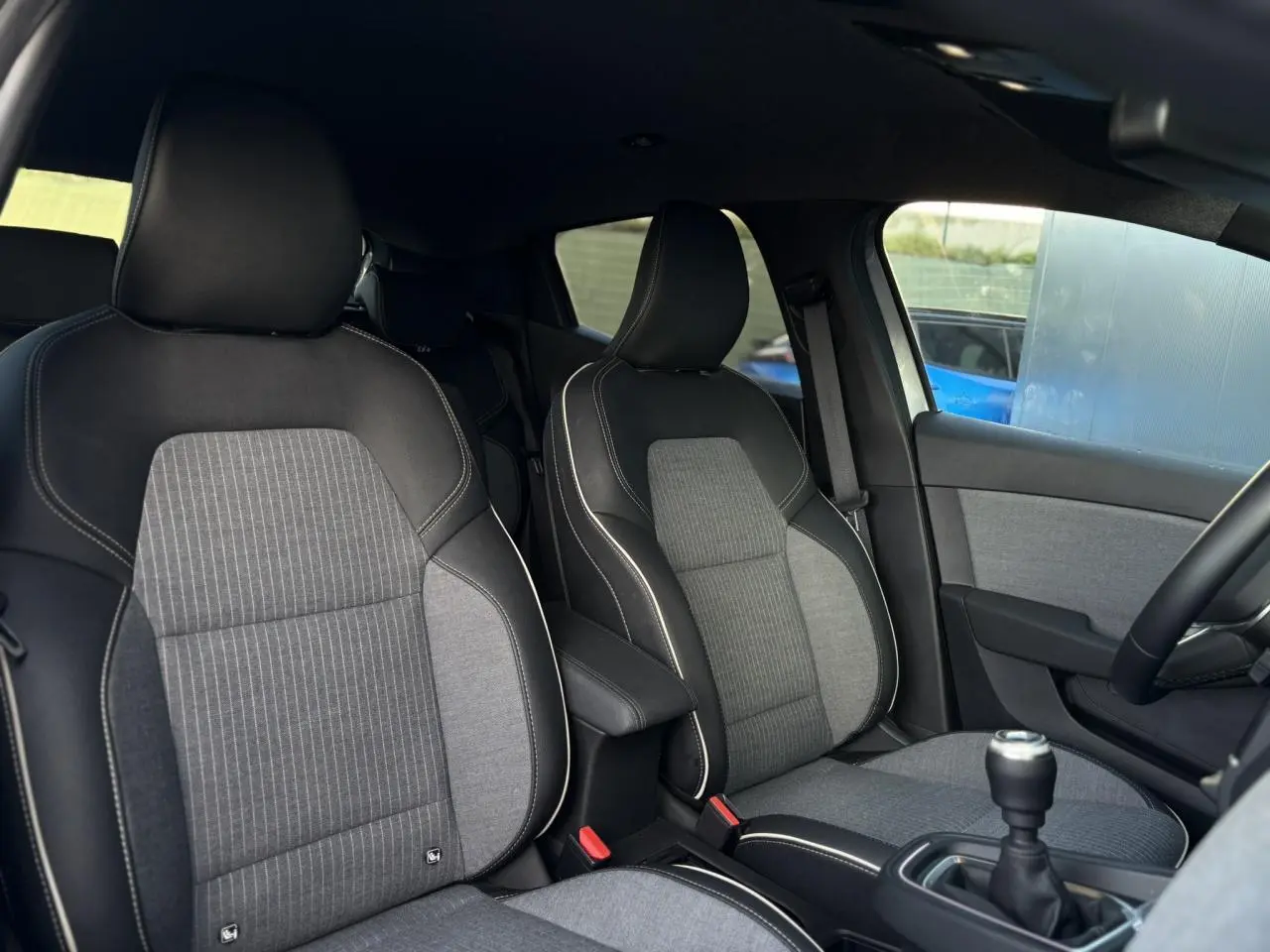 Vue intérieure des sièges avant en tissu gris et noir de la Renault Clio V TCE 90 Techno avec boîte manuelle.